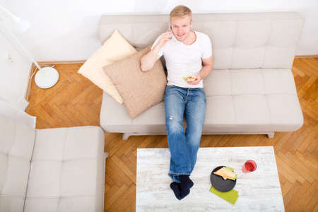 Young man with a Sandwich on the Sofa while talking on the phone.
の写真素材