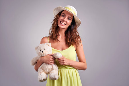 A beautiful young woman smiling and holding a teddybear in a green dress and a hatの写真素材