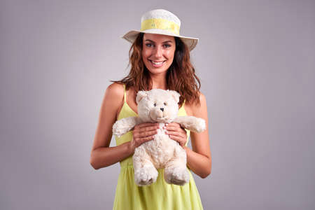 A beautiful young woman smiling and holding a teddybear in a green dress and a hatの写真素材