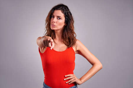 A serious young woman pointing in to the camera in a red topの写真素材