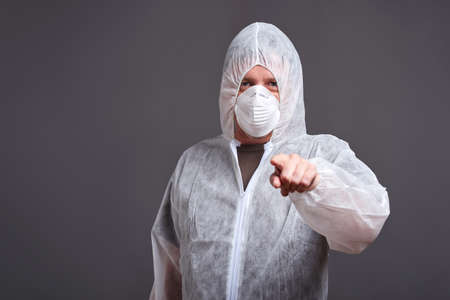 A middle aged man standing in a mask with the hoods on of the clothes protector suit and pointing to the cameraの写真素材