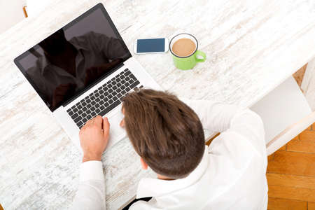 A young man sitting at the table with a laptop and coffee.
