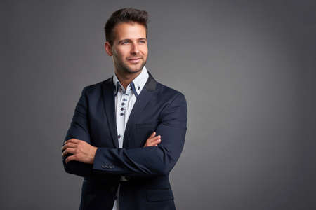 A confident elegant handsome young man standing in front of a grey background in a studio