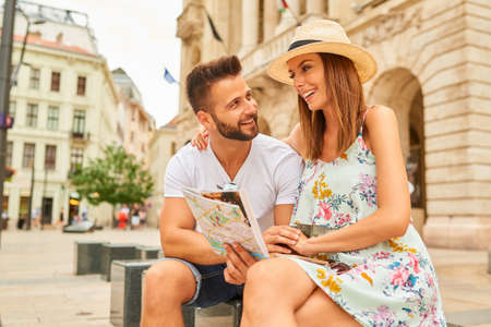 A beautiful young couple are sitting and holding a map and looking around at the Egyetem Square in Budapest, Hungary.の写真素材