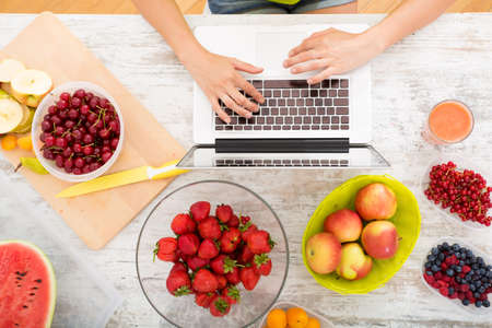 A beautiful mature woman using a Laptop computer in the kitchen with fruits.の写真素材