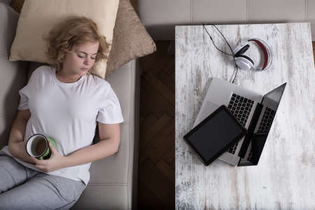 A young plus size woman falling asleep at night on the sofa with a Tablet PC and a Laptop on the Table.の写真素材