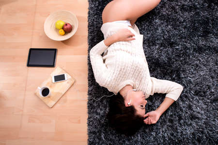 A young beautiful woman in underwear lying on a carpet and listening to musicの写真素材