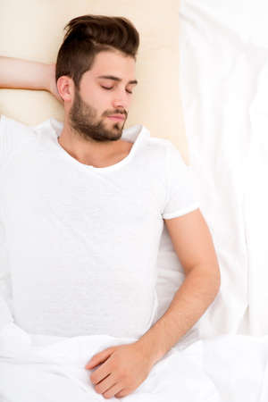 A handsome young adult man sleeping in bed.の写真素材