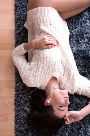 A young beautiful woman in underwear lying on a carpet and listening to musicの写真素材