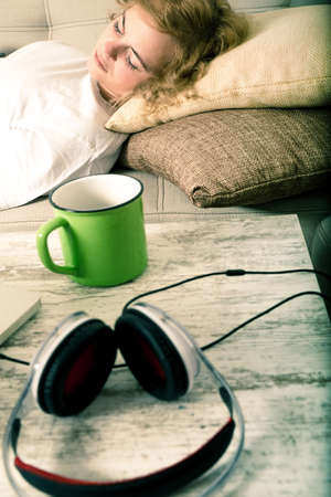 A young plus size woman sleeping on the sofa with headphones on the Table.の写真素材