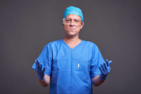 A middle aged male doctor in blue scrubs taking his gloves on and getting ready