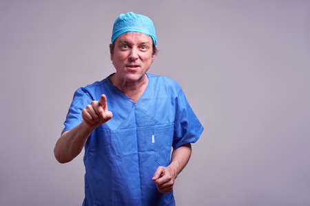 A middle aged male doctor pointing in to the camera in a blue scrubの写真素材