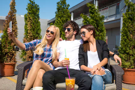 Friends siting on the terrace of a coffee shop and taking a selfie