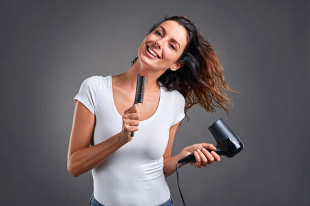 A beautiful young woman feeling happy and singing while using a hairdryer and a hairbrush.の写真素材