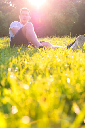 A handsome young man relaxing in the sunset and sitting in the grass.の写真素材