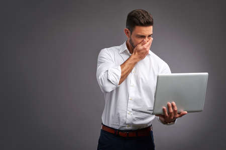 A handsome young man feeling confused while looking at a laptop in a white shirtの写真素材