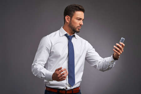 A handsome young man feeling upset while holding and looking at his smartphoneの写真素材