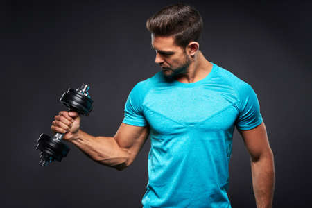 A handsome young sportsman lifting a dumbbell with one hand