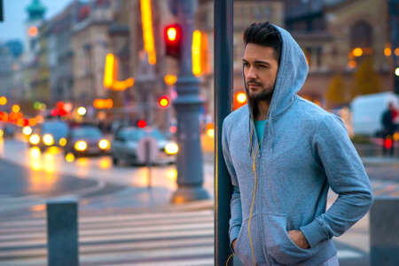 A handsome young sportsman leaning to a pillar on the street with the car lights behind himの写真素材