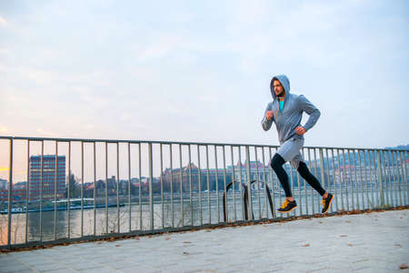 A handsome young man running in the sunset next to a fence on the riversideの写真素材