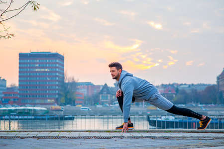 A handsome young man stretching and warming up on the riverside with the sun setting behind himの写真素材