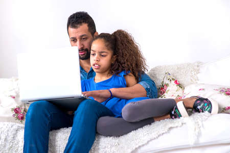 Black father and his daughter siting on a couch with a laptopの写真素材