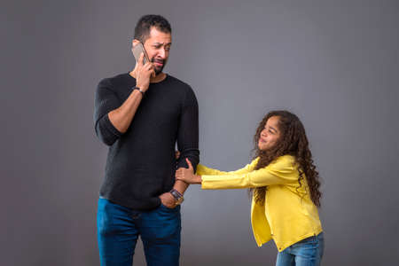 Black father talking on his phone while his daughter pulling hisの写真素材