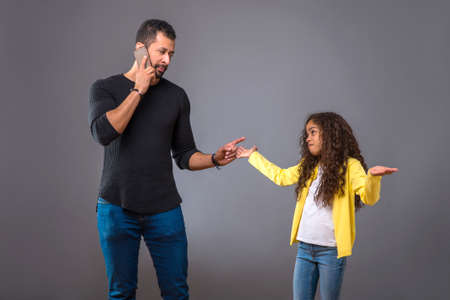 Black father talking on phone while his daughter looking questioの写真素材