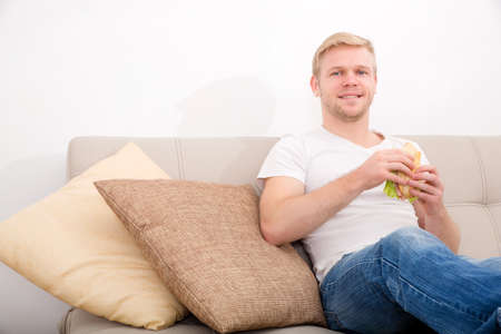 A young adult man eating a sandwich at home on the couch.
の写真素材