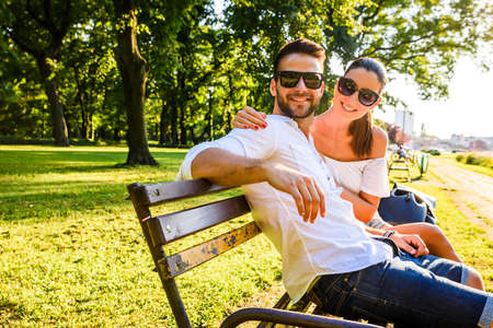 Beautiful young couple relaxing on a sunny summer day on a benchの写真素材
