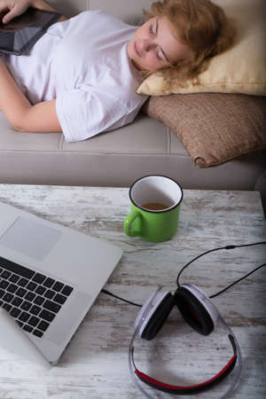 A young plus size woman falling asleep at night on the sofa with a Tablet PC and a Laptop on the Table.の写真素材