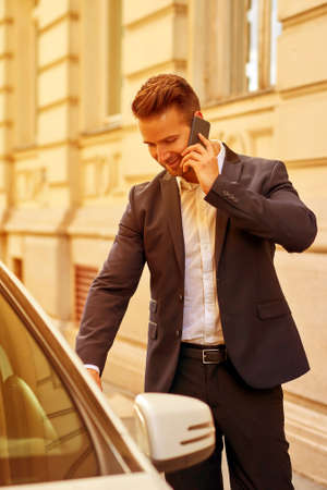 Young businessman walking to his car and talking on a phoneの写真素材