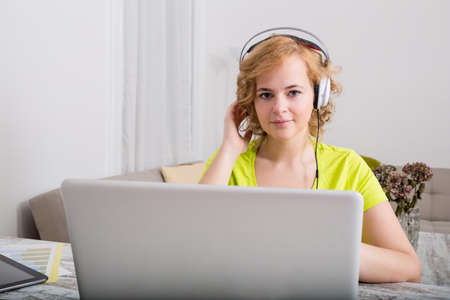 A young plus-sized woman sitting at home in front of a laptop computer while listening to music in the evening.の写真素材