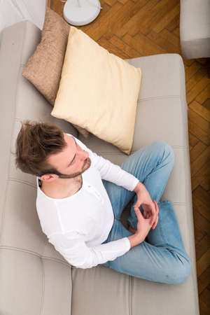 A young man meditating on the sofa in the living room.の写真素材