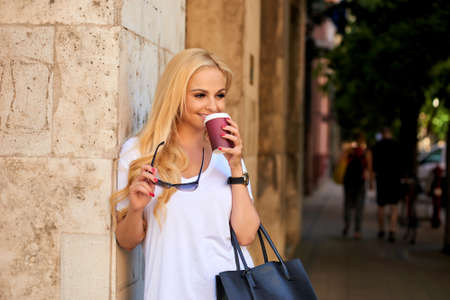 Young woman at the wall on the street with coffeeの写真素材