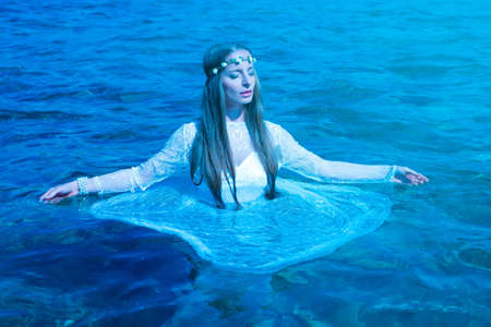 Young woman standing in the ocean at nightの写真素材