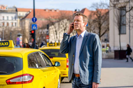 A middle age businessman waiting and looking for an empty taxi at the taxi station while talking on his phoneの写真素材