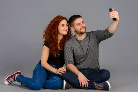 A beautiful young couple sitting on the floor in a studio and taking a selfie with a smartphoneの写真素材