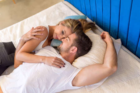 A beautiful young couple laying on the bed and cuddling.