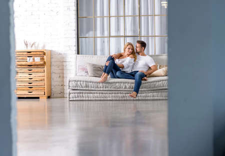 A beautiful young couple sitting on the sofa and cuddling.の写真素材