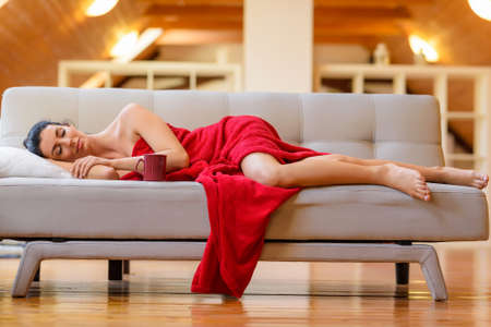 A beautiful nude woman wrapped in a cozy blanket relaxing on theの写真素材