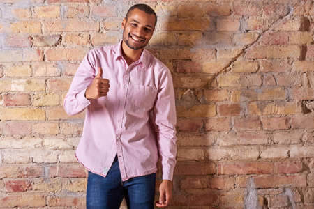 A handsome young man showing thumbs up in a pink shirt.の写真素材