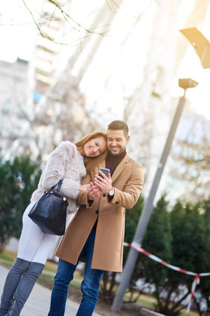A beautiful young couple taking a selfie on the street with christmas trees in the background.の写真素材