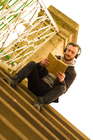 A retro style photo of a young hipster man sitting on the stairs and reading a book.