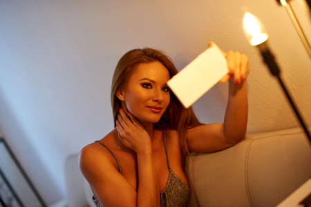 A young woman taking a selfie on a sofa in a night dressの写真素材