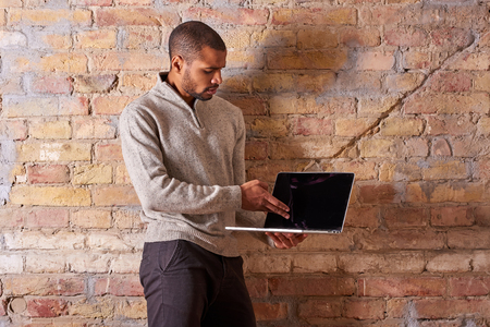 A serious handsome young man pointing to the screen of his laptop in a sweater.の写真素材