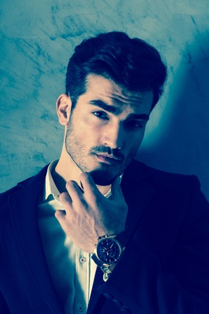 Portrait of a thinking handsome businessman in a black suit in front of a grey wall in a studio.の写真素材