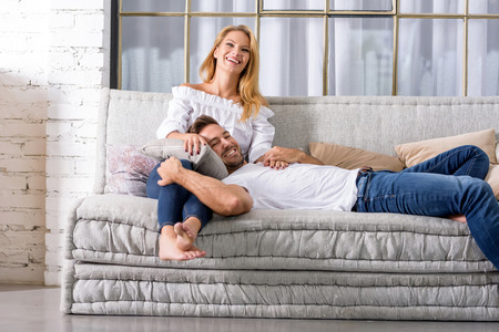 A handsome young man lying on the sofa with head on his girlfriends chest.の写真素材