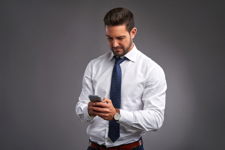 A handsome young man feeling upset while holding and looking at his smartphoneの写真素材