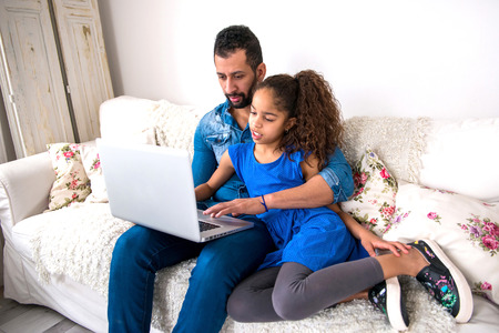 Black father and his daughter siting on a couch with a laptop